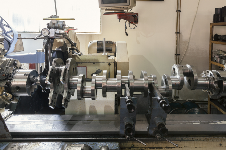 Heavy equipment crankshaft being repaired on a workbench during a major engine rebuild