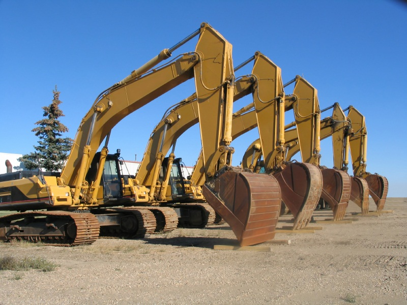 Used excavators lined up at auction representing used heavy equipment buying decisions, machine inspections, and ownership cost